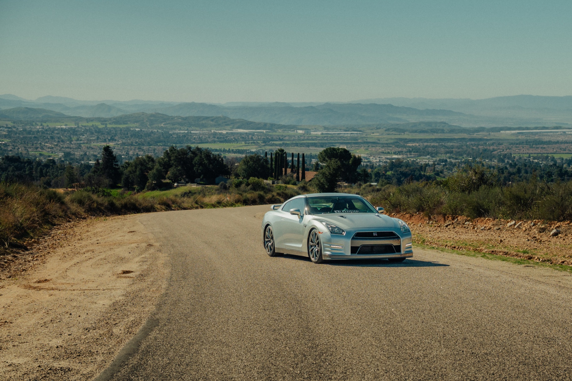 Silver Nissan GT-R on a hilltop road overlooking Beaumont valley